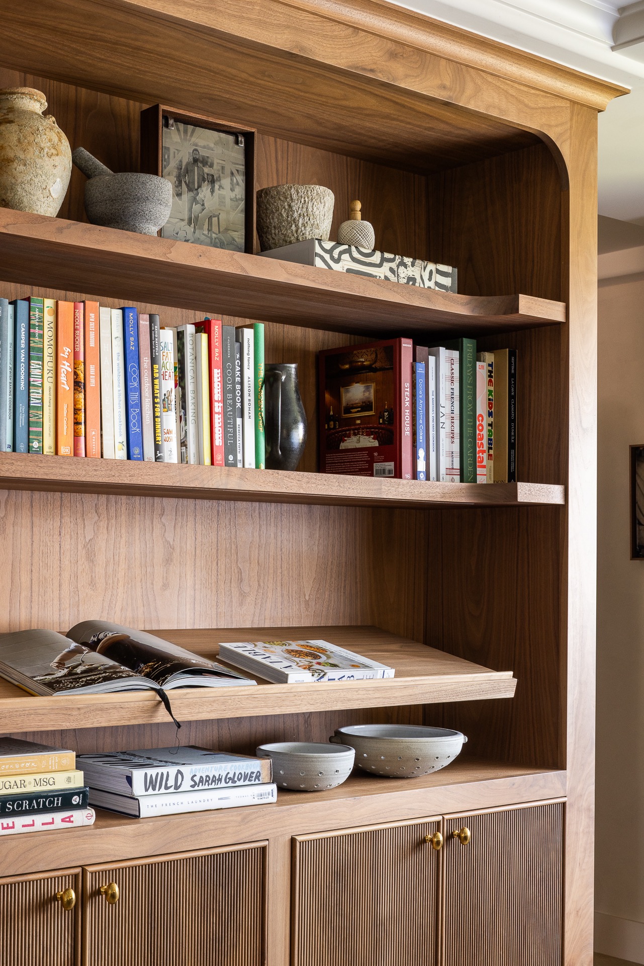 Walnut bookshelf layered with cookbooks, pottery and personal objects